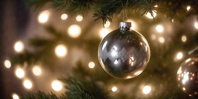 The primary subject of the image is a silver Christmas ornament hanging from a tree. The ornament is shiny and reflective, adding a touch of elegance to the scene. The setting is a Christmas tree, which is adorned with lights, creating a festive atmosphere. The visual style of the image is a close-up of the ornament, highlighting its details and reflective surface. The colors and mood of the image are predominantly silver and white, with the lights adding a warm and inviting touch